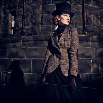 Female young adult in period clothing wearing black hat and veil with Harris tweed jacket and gloves holding riding crop