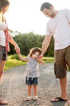 little girl holding on to mom and dad\'s hands