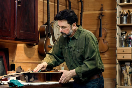 Middle aged man working on a guitar in a restoration shop