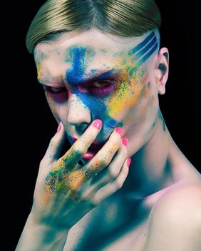 Young woman, naked, touching face, colourful powder and paint on face
