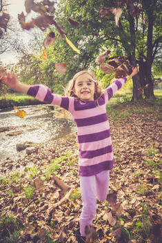 Little girl throwing autumn leaves