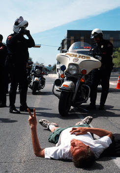 Two uniformed police officers with a motorbike stand over a protester lying on the road, Austin, Texas, USA.