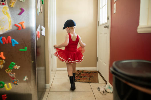 Grant, a young red-head boy, runs and plays while wearing his older sister Jane\'s red ballet tutu walking through the kitchen of his family\'s suburban home. Denver, Colorado