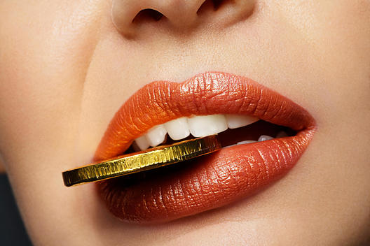 Close up beauty shot of a girl with a gold wrapped chocolate coin between her teeth
