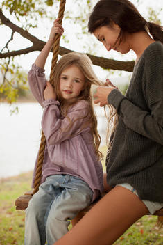 Mother braiding daughter?s hair on swing at lakeside