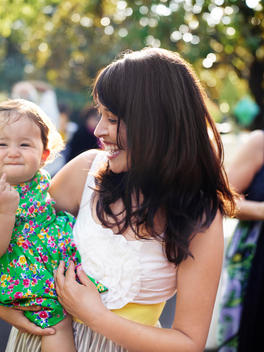Woman holding a baby girl, both dressed up for a special event.