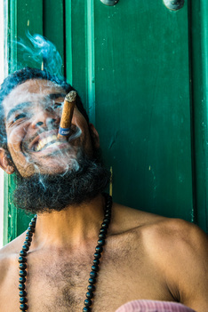 A bearded young Cuban artist happily smokes a Montecristo cigar in a Fidel Castro-like pose. Trinidad, Cuba