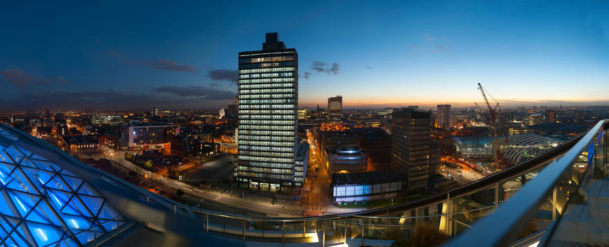 A roof top shoot of Manchester at night time, with the towers of the city lit up.