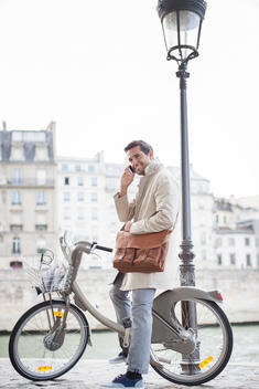 Businessman talking on cell phone on bicycle along Seine River, Paris, France
