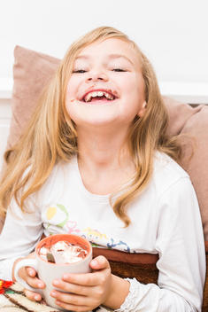 Smiling little girl covered with chocolate holding cup of cacao, studio shot