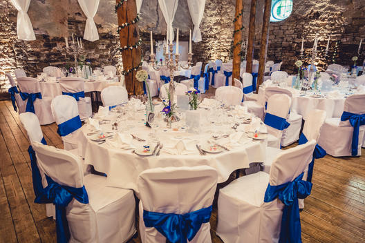 decorated wedding room, vintage stone wall, big chandelier, white covered chairs with a blue loop