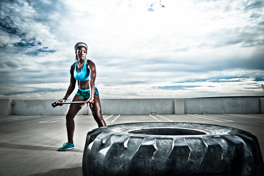 An athletic girl works out with a sledgehammer and a large tire.