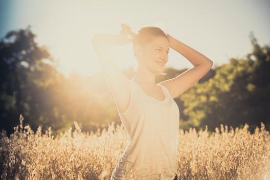 young woman standing and smiling at summer in a cornfield, back light and lens flare