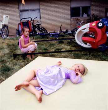 Friends Play Amidst Styrofoam Mattress, Bikes, And Other Things Strewn On Front Lawn