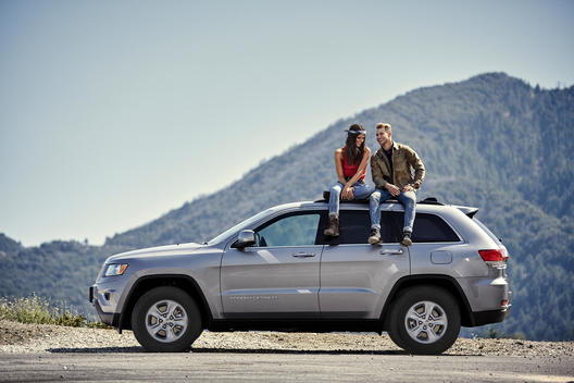 Male and female model sitting on top of Jeep roof laughing with mountains in the background.