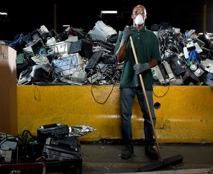A worker wearing a mask is sweeping in front of a pile of recyclables at a plant