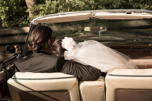 Bridal couple sitting in vintage car convertible, back view
