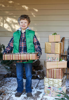 Boy holding Christmas gifts on snowy porch