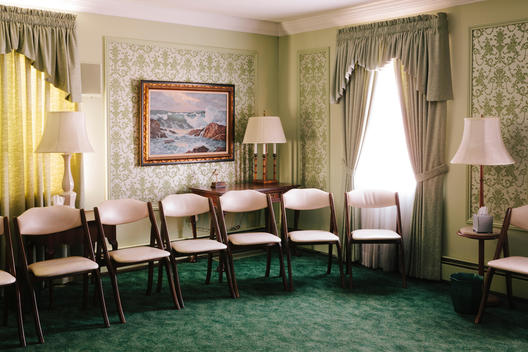 Padded white folding chairs in a green wallpapered room of a funeral home.