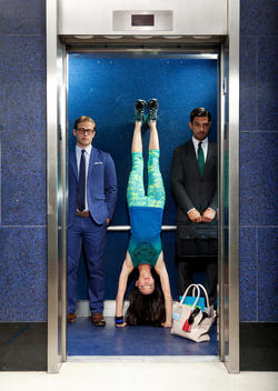 A young woman does a handstand inside an elevator in between two businessmen