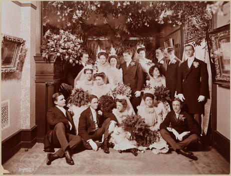 What May Be The Living Room Of The Residence Of Miss Harper On The Occasion Of Her Wedding. The Wedding Party Surrounds Her, Both Seated On The Floor And Standing. Flower Arrangements, Fireplace And Paintings On The Walls Are Visible.