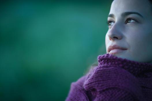 Woman pulling sweater up to face, looking away, close-up, cropped