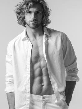 Male model with long hair, shirt open and white pants