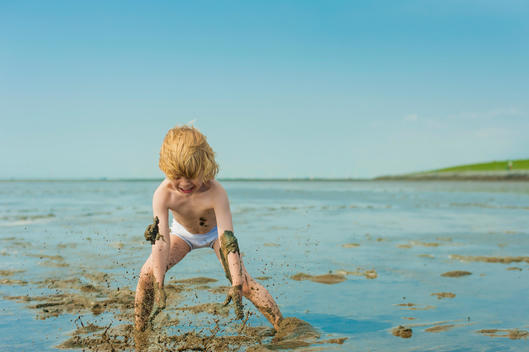 Germany, Schleswig Holstein, Boy playing in mud at beach