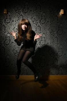 Woman Jumping And Doing Jazz Hands Pose Against Elaborate Wallpaper