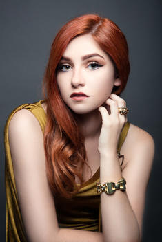 Beauty fashion portrait with a luxury aesthetic of a woman with red hair wearing gold dress and gold jewelry.