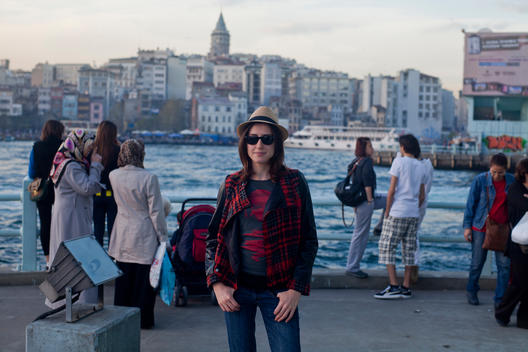 Young Turkish woman poses in front of a famous Galata Tower, this area is under the Galata Bridge in Istanbul, Turkey.