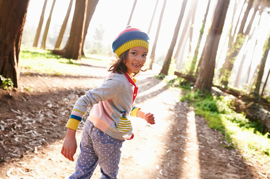 girl walking and smiling in a wood with sunbeam coming trough the trees