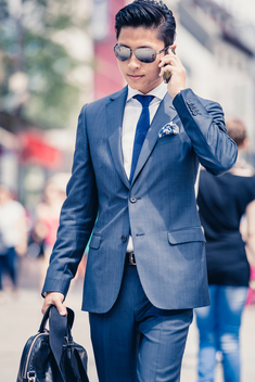 Asian businessman with leather bag, cell phone and sunglasses walking through the city