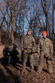 Two hunters pose for a photograph in full camouflage in the woods on a fall day.