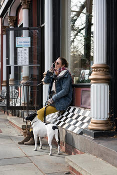 Young smiling seated woman with dog on cell phone wearing denim jacket
