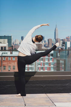 A young female dancer holding a dance pose with the iconic Empire State Building in New York City.