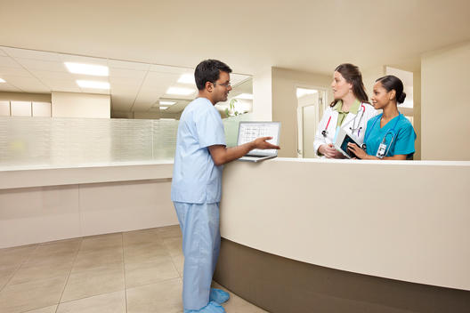 Indian male doctor with laptop computer having a conversation with a female doctor and african american female nurse, at the reception desk in a medical office.
