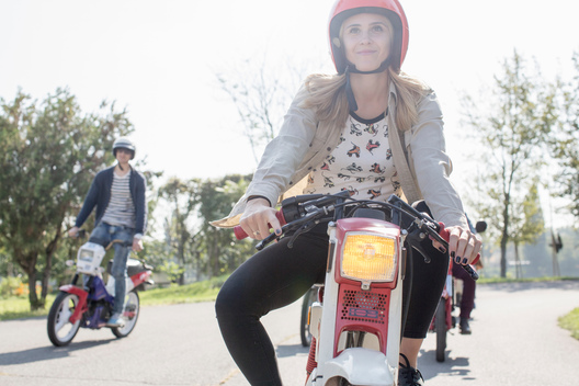 Group of friends riding mopeds along road, young female rider in foreground