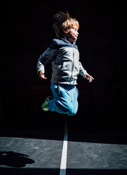 6 year old blonde boy in blue pants jumping in hard light with dark background.