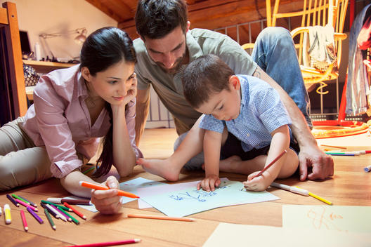 Boy sitting on floor drawing with parents