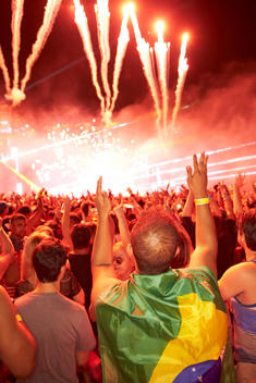 A man with a Brazilian flag as a cape with fireworks in the background.