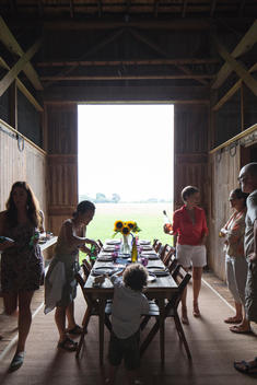 People standing around dinner table inside a barn at Tom Colicchio's farm
