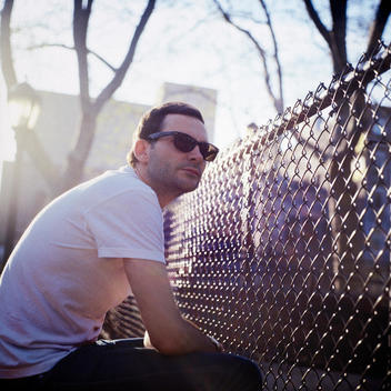 Man in a white t-shirt and sunglasses in front of chain link fence