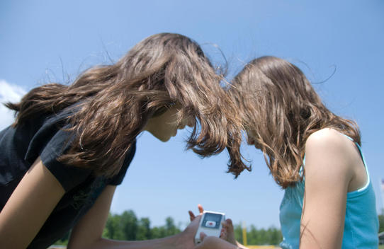 Two Young Sisters Look Onto A Handheld Video Device Happily. - Stock ...